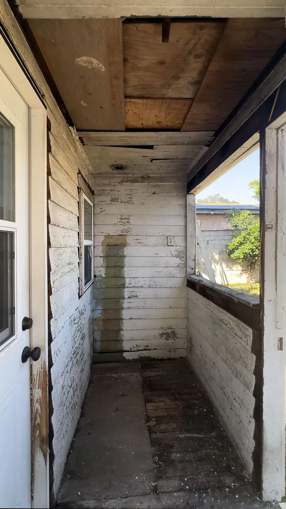 Back porch before: peeling paint, exposed rough ceiling, and rotted floorboards