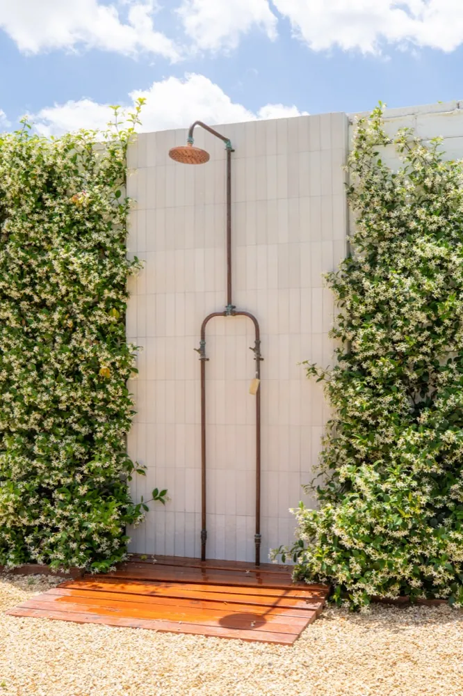 Finished outdoor shower with copper fixtures surrounded by jasmine