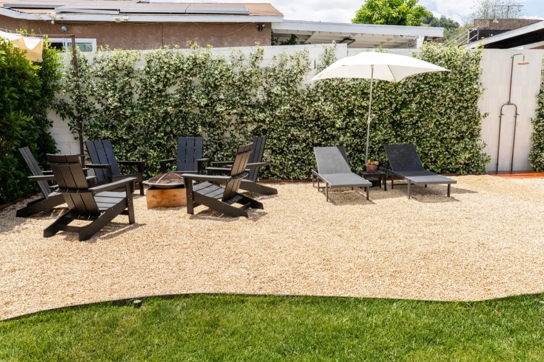 Gravel patio with lounge chairs, umbrella, and lawn edge